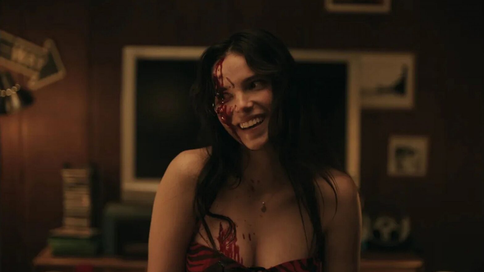 Young woman with blood on her face and chest, smiling in a dimly lit room.
