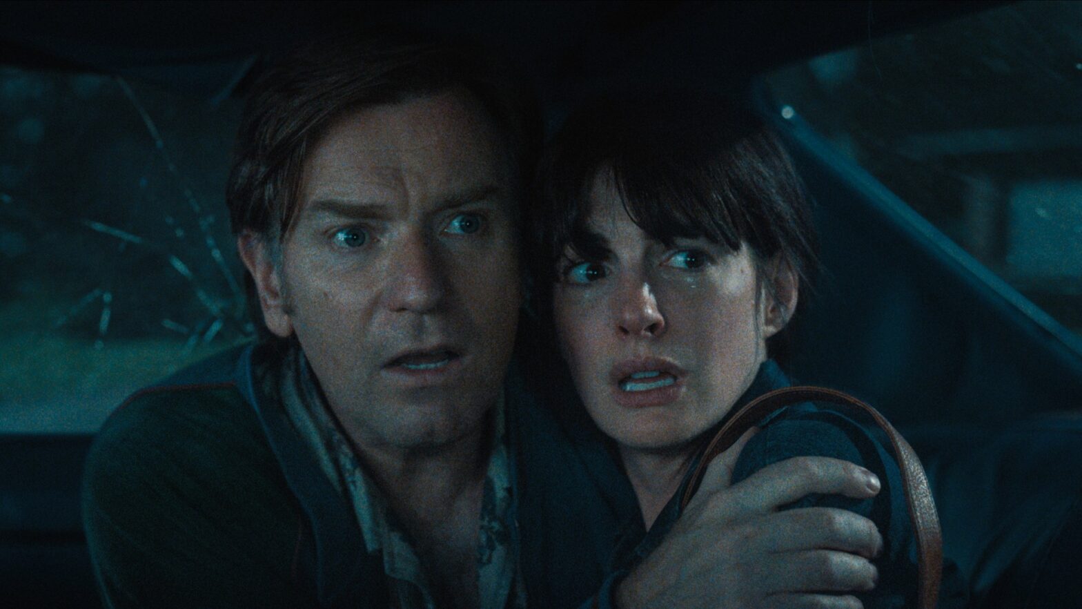 Man and woman huddle close in a car, eyes wide with fear as they look toward something off-screen.